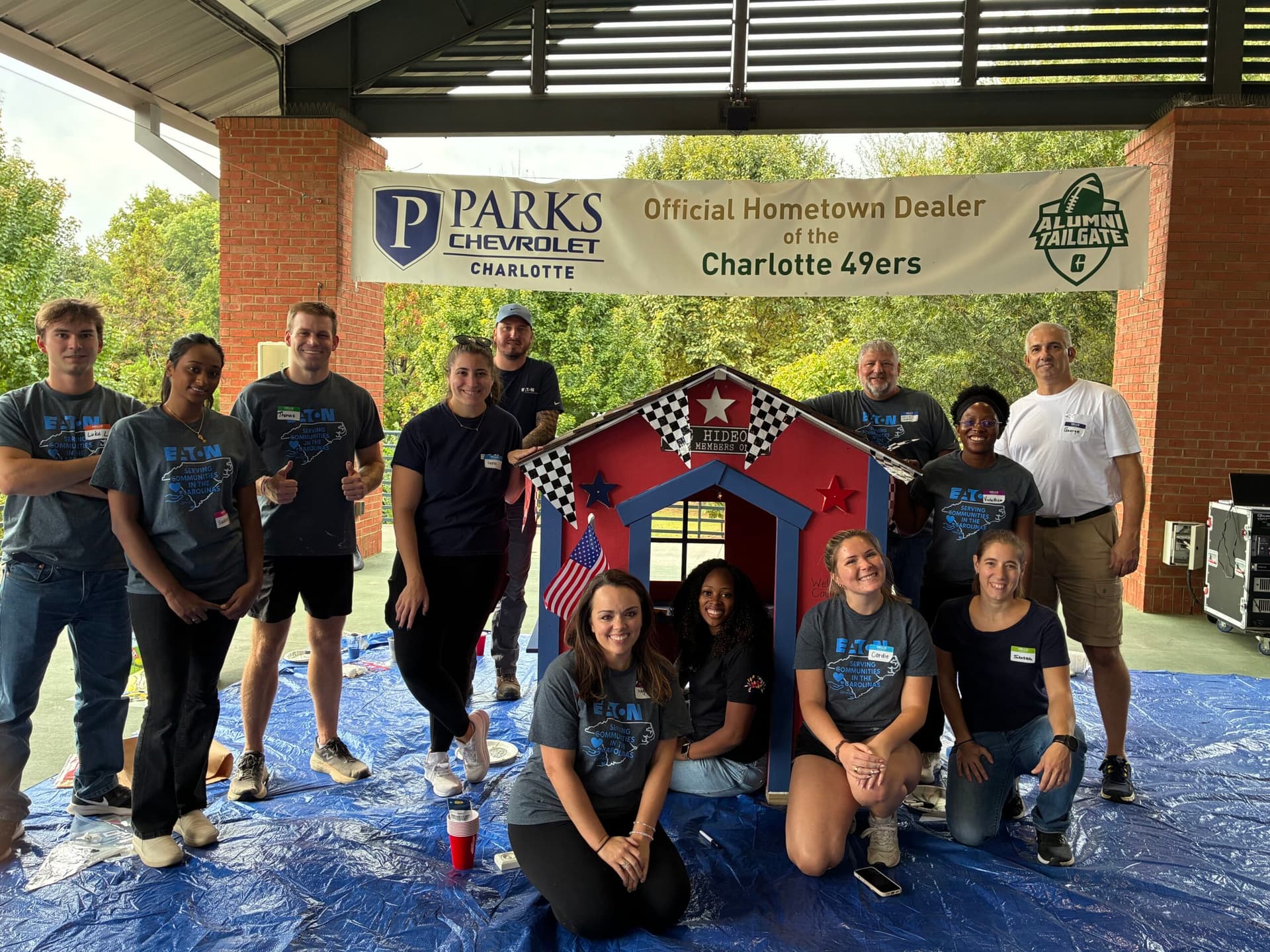Volunteer group posing in front of red and blue playhouse